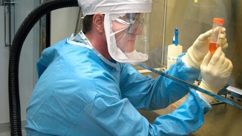 Researcher in protective clothing handling a vial