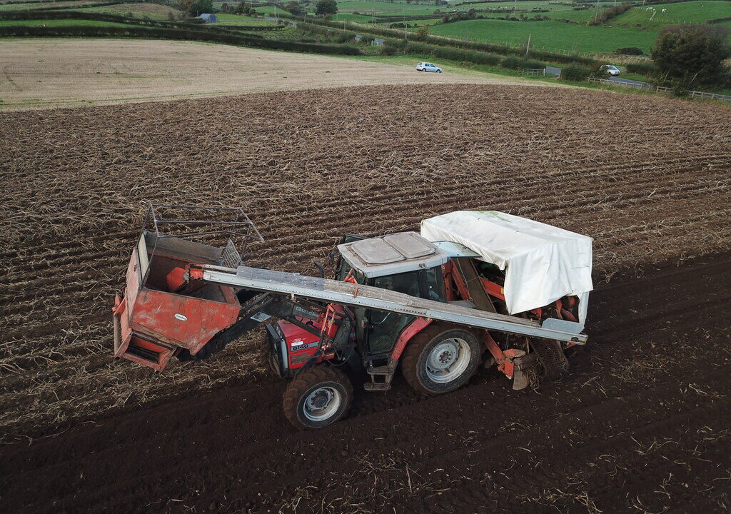 Tractor harvesting a ploughed field under green hills