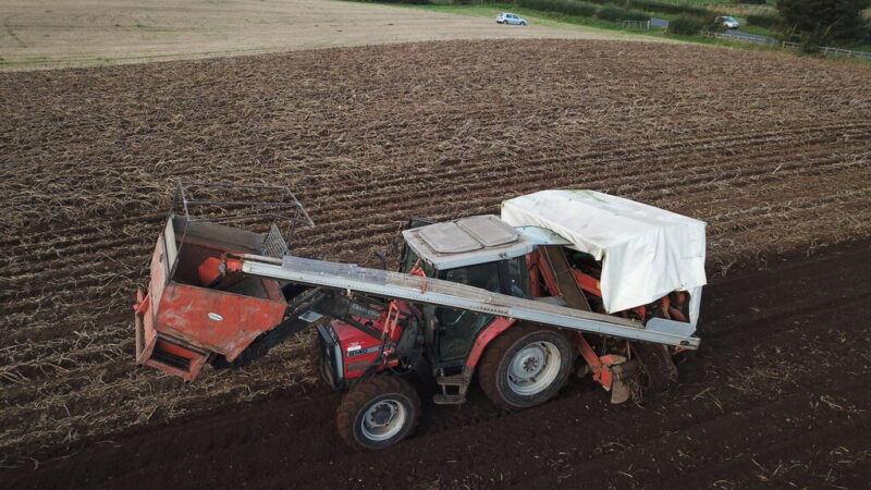 Tractor harvesting a ploughed field under green hills